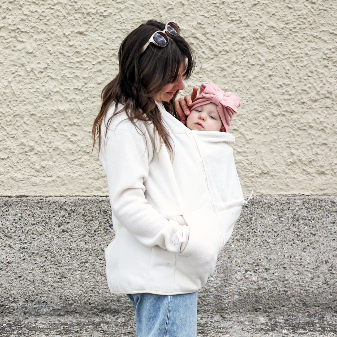 Maman portant bébé sous une veste de portage en polaire claire, moment tendre