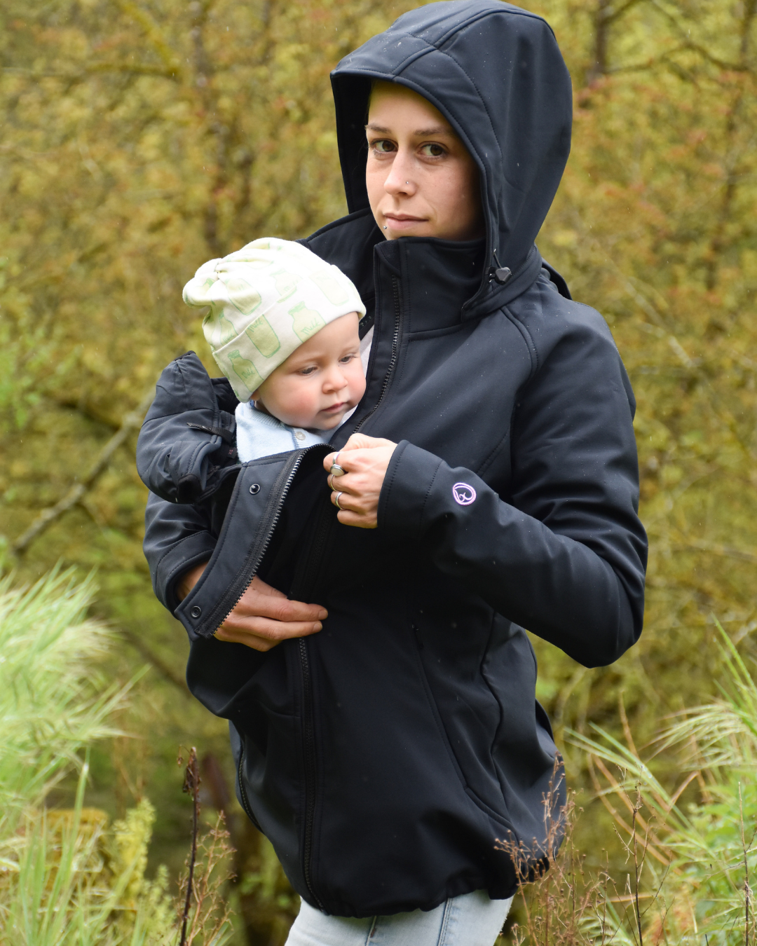 Femme portant bébé sous veste noire à capuche en nature automnale