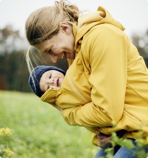 Une jeune maman portant un gilet de portage jaune softshell avec son bébé.