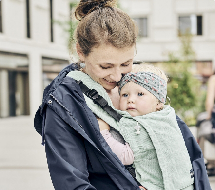 Eine junge Mama mit Tragelatzhose liebkost ihr Baby.