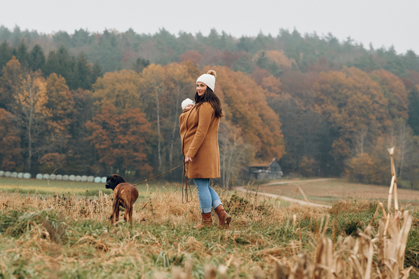 Femme avec bébé en manteau de portage, chien en laisse, paysage automnal