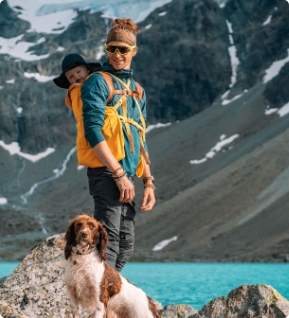 Père portant bébé sur le dos avec chien au bord d’un lac de montagne