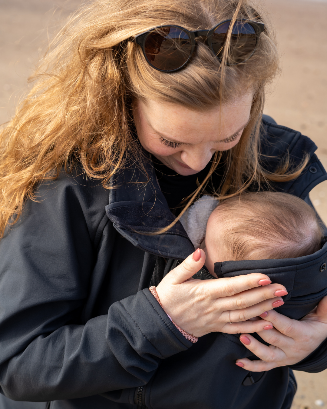 Femme portant bébé contre elle dans veste sombre en extérieur